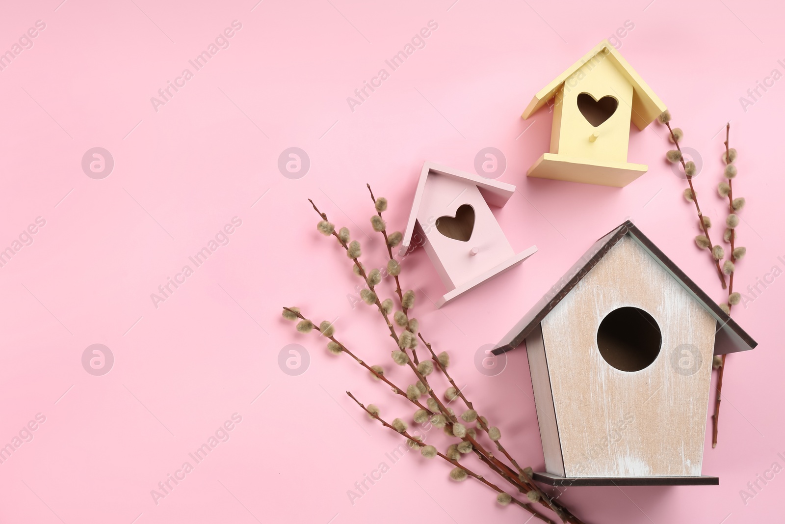 Photo of Beautiful bird houses and pussy willow branches on pink background, flat lay. Space for text