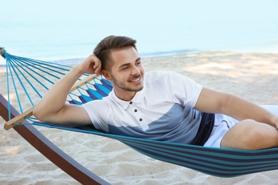 Photo of Young man relaxing in comfortable hammock at seaside