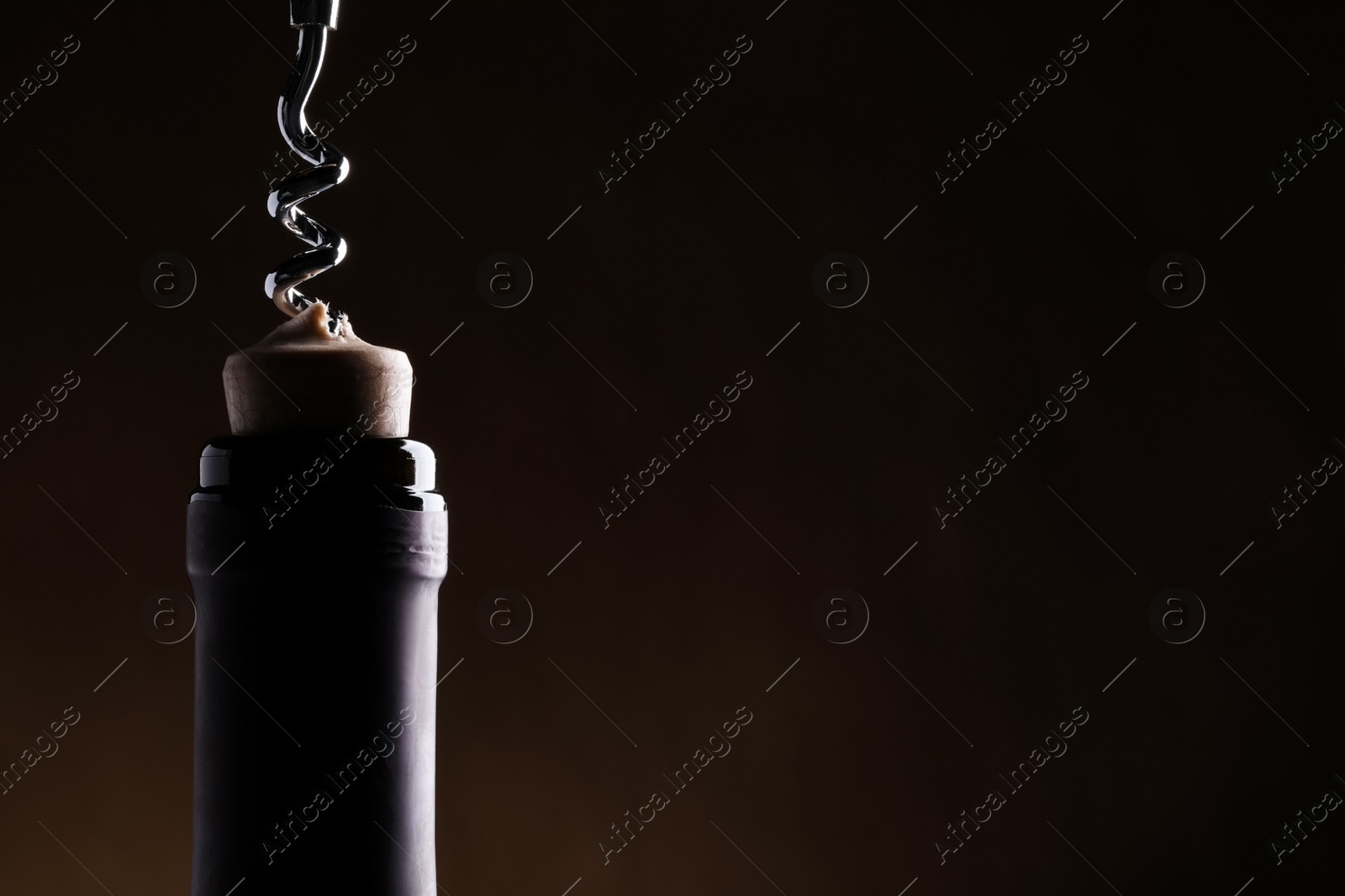 Photo of Opening wine bottle with corkscrew on dark background, closeup. Space for text