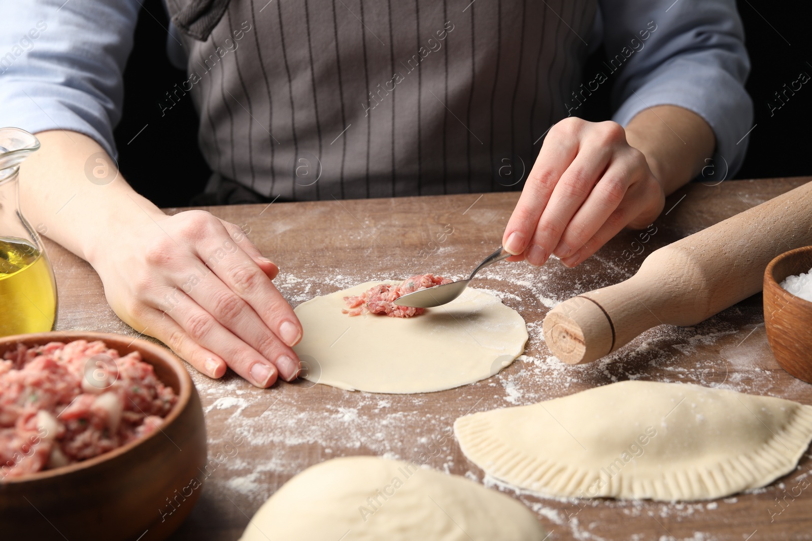 Photo of Woman making chebureki at wooden table, closeup