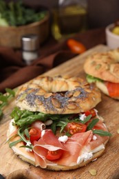 Photo of Tasty bagel with cured ham, cream cheese, tomatoes and arugula on table