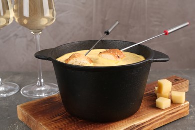 Photo of Fondue pot with tasty melted cheese, forks, bread and wine on grey table