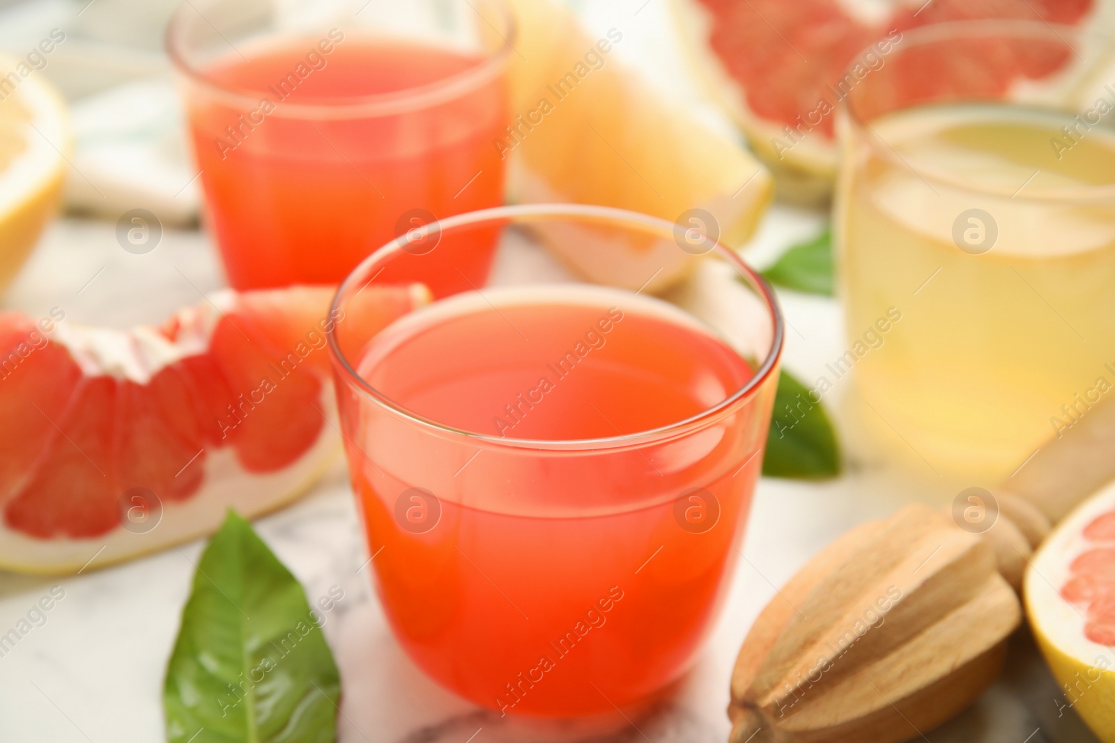 Photo of Glass of pink pomelo juice and reamer on white marble table, closeup