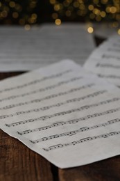 Photo of Closeup view of note sheets on wooden table against blurred lights. Christmas music