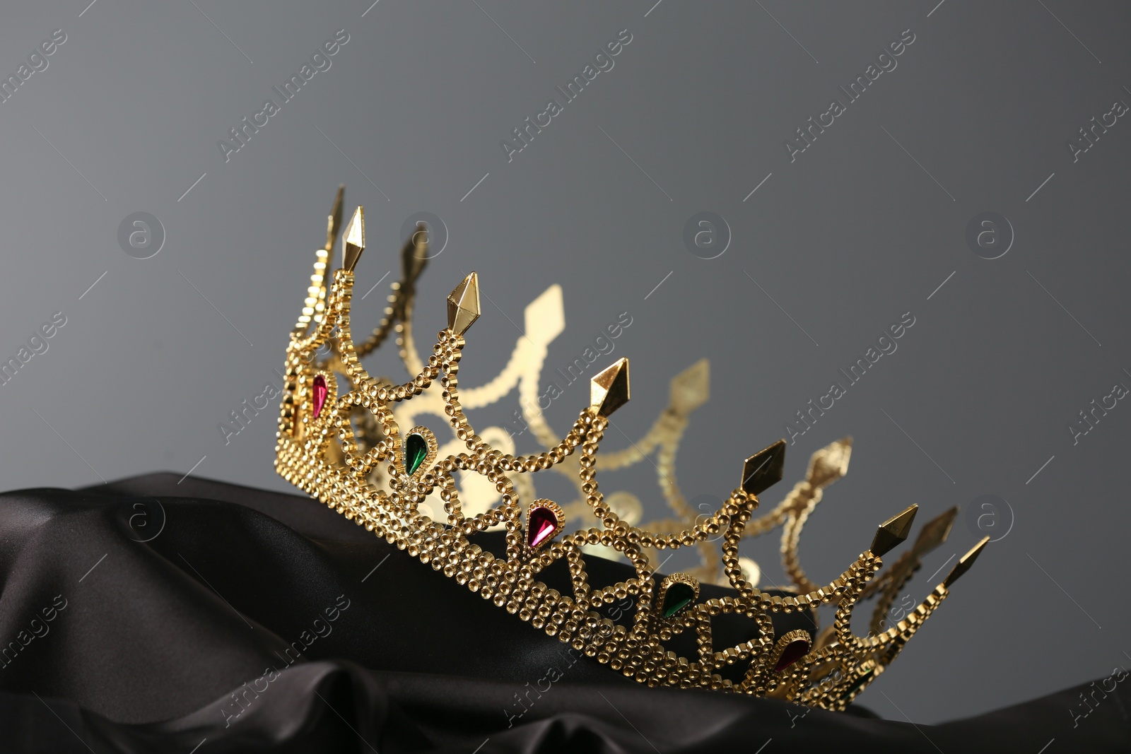 Photo of Beautiful golden crown with gems on dark cloth against grey background