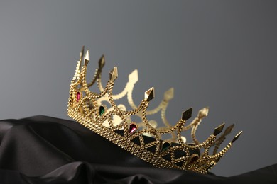 Beautiful golden crown with gems on dark cloth against grey background