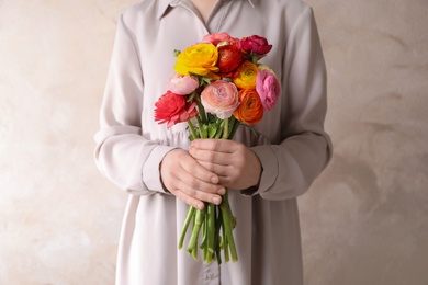 Photo of Woman holding beautiful ranunculus flowers against beige background, closeup
