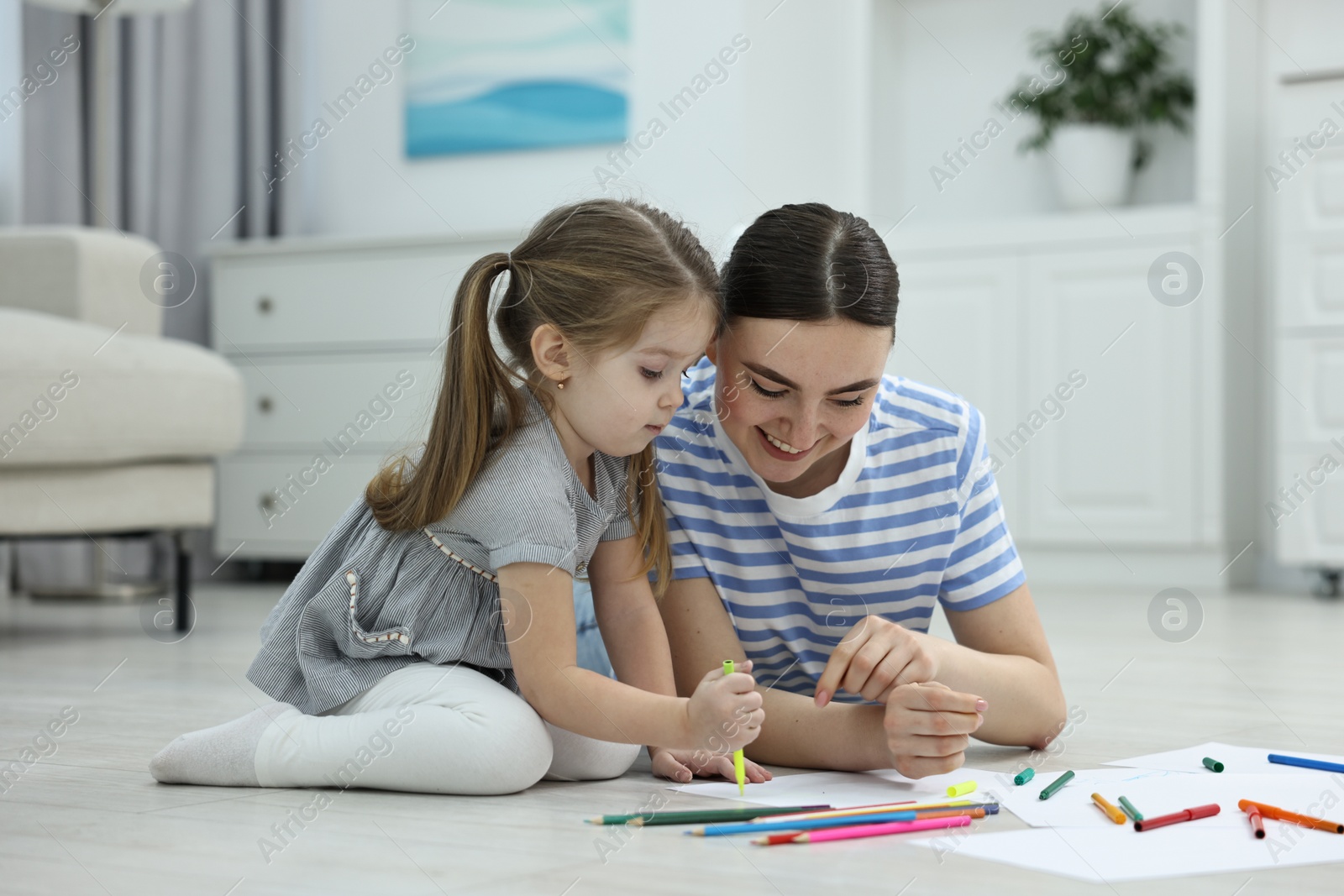 Photo of Mother and her little daughter drawing with colorful markers on floor at home