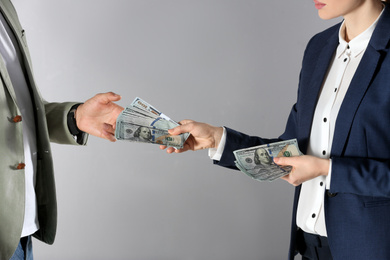 Photo of Woman giving bribe money to man on grey background, closeup