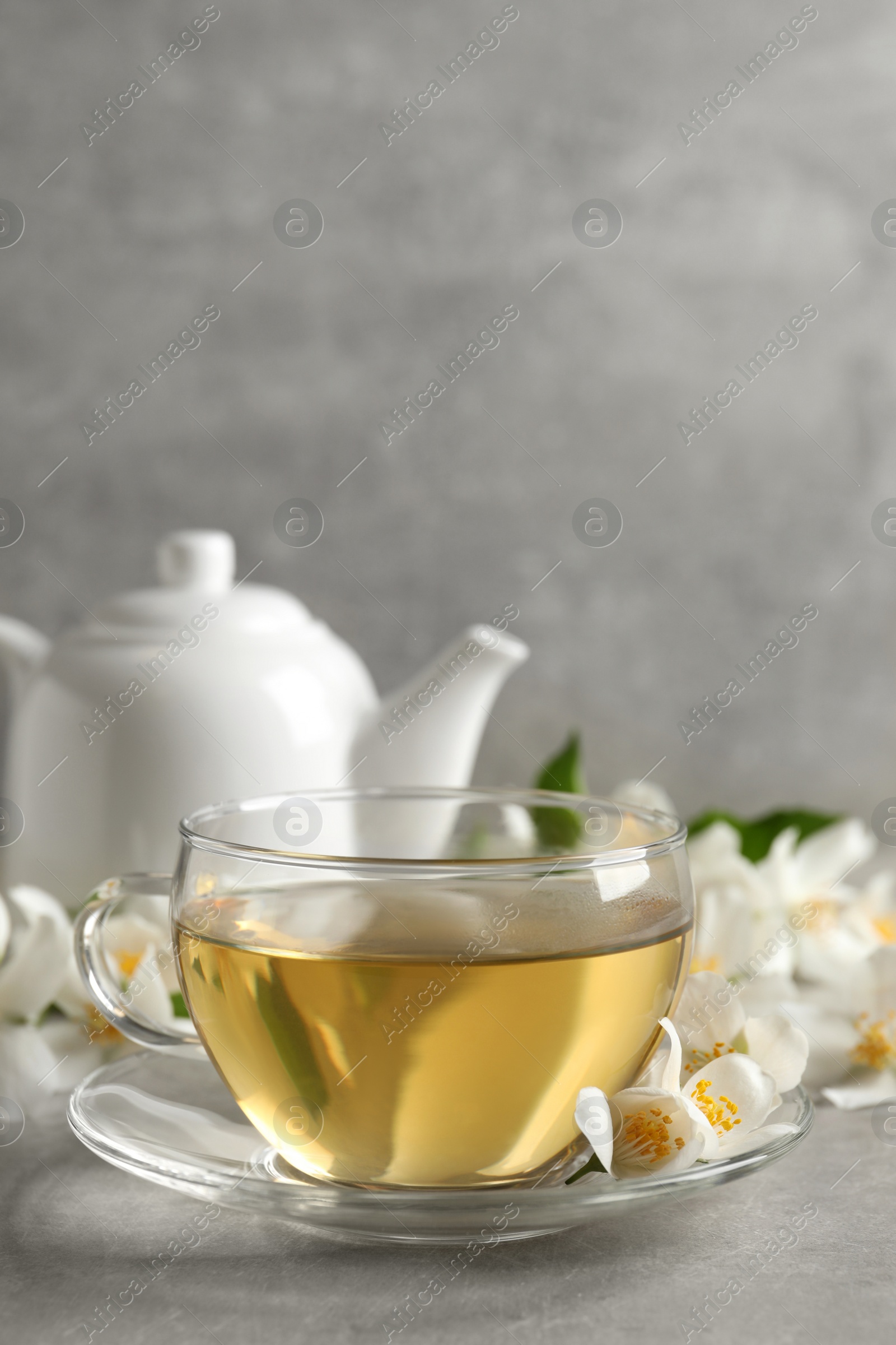 Photo of Glass cup of jasmine tea and fresh flowers on grey table