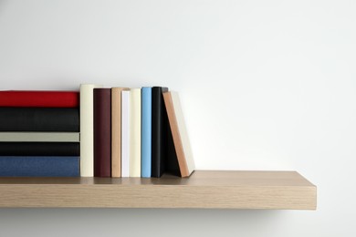 Many hardcover books on wooden shelf near white wall. Space for text