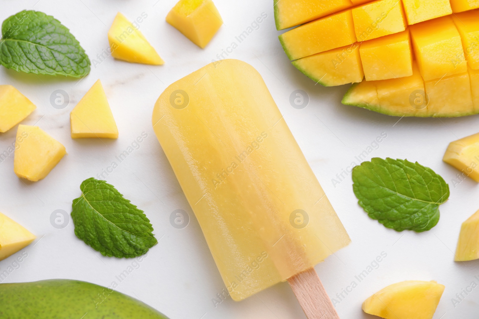 Photo of Tasty mango ice pop on white marble table, flat lay. Fruit popsicle