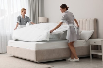 Professional chambermaids making bed in hotel room