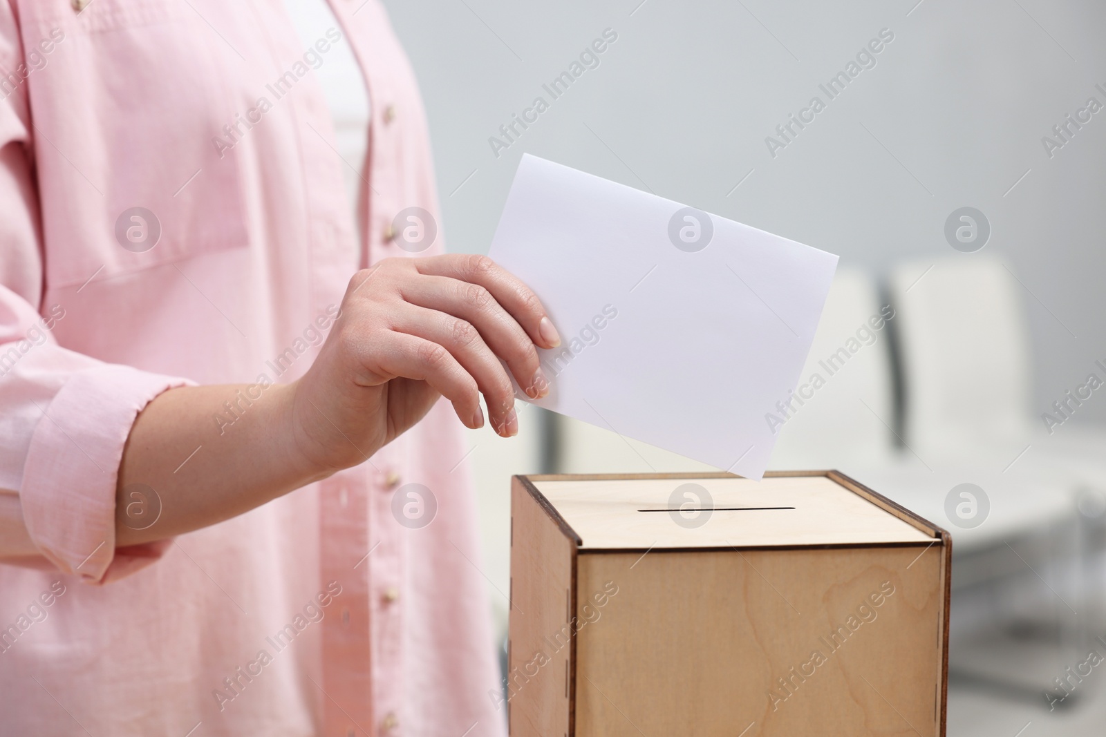 Photo of Woman putting her vote into ballot box on blurred background, closeup