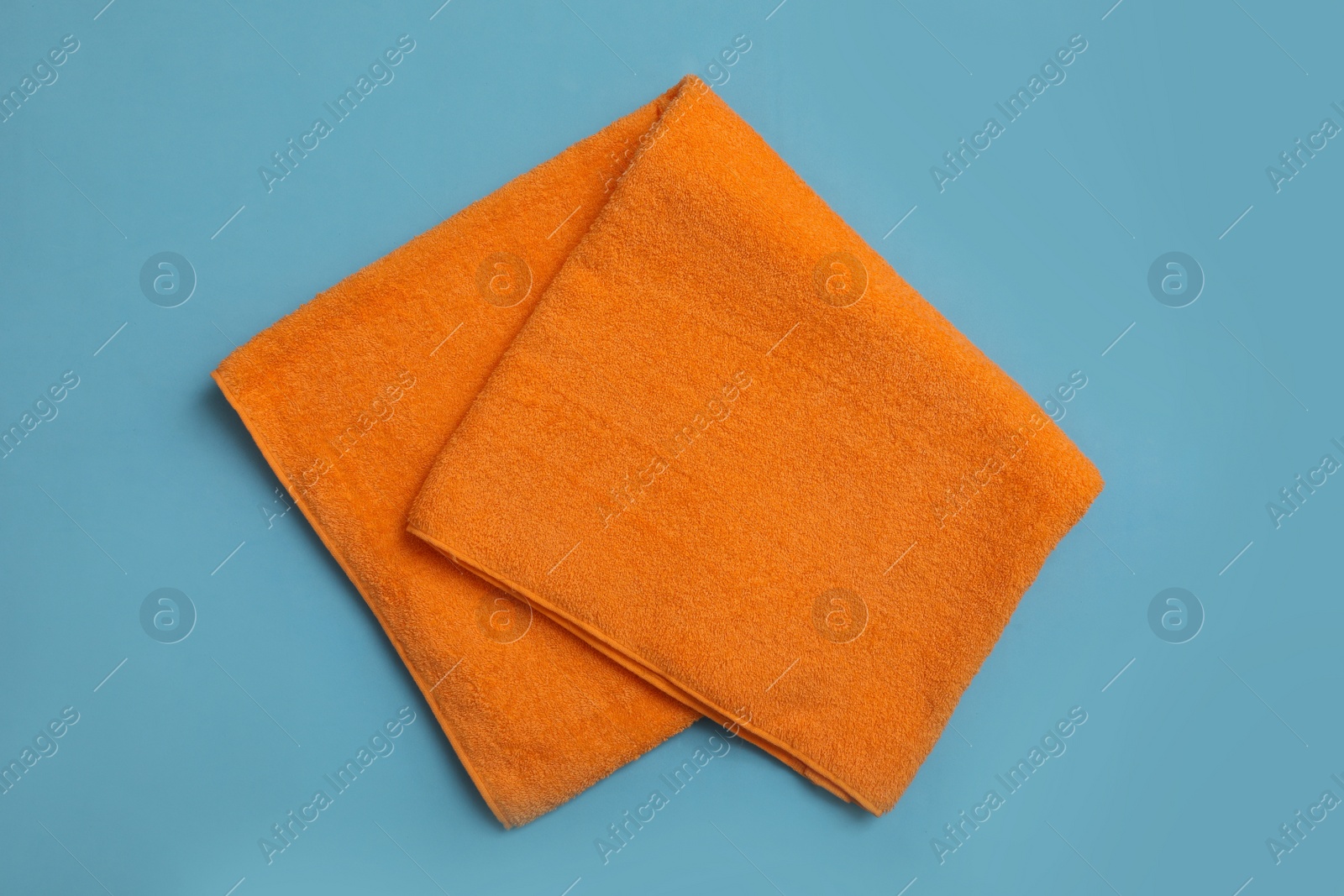 Photo of Folded orange beach towel on light blue background, top view