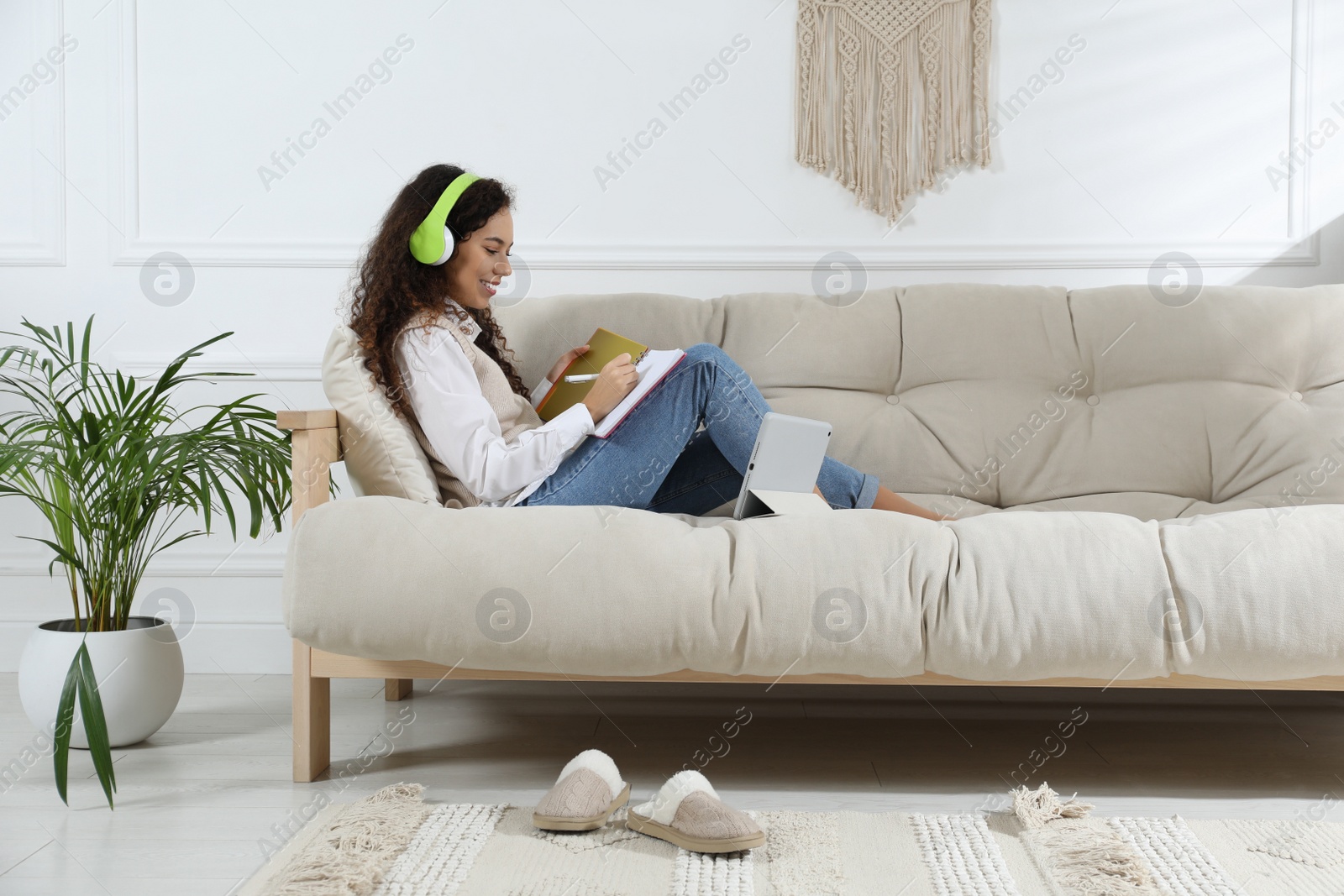 Photo of African American woman with headphones and tablet studying on sofa at home. Distance learning