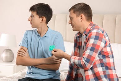 Photo of Father giving condom to his teenage son in bedroom. Sex education concept