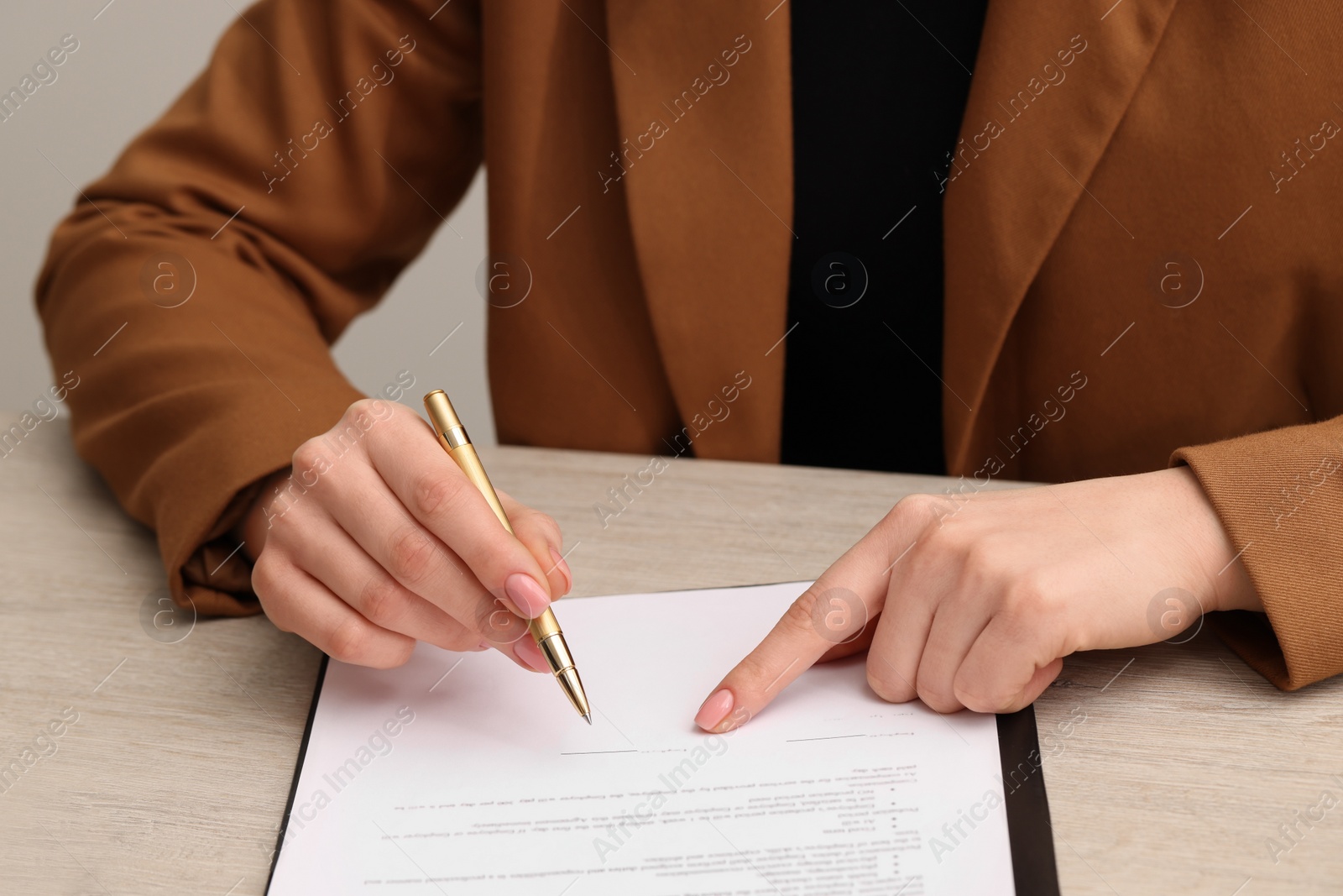 Photo of Woman signing document at wooden table, closeup