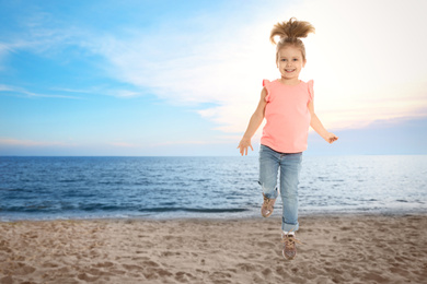 Image of Happy school girl jumping on beach near sea, space for text. Summer holidays
