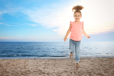 Happy school girl jumping on beach near sea, space for text. Summer holidays