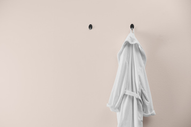 Soft comfortable bathrobe hanging on beige wall, space for text