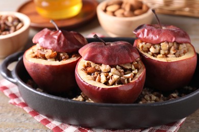 Tasty baked apples with nuts in baking dish on table, closeup