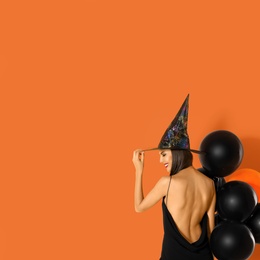 Beautiful woman wearing witch costume with balloons for Halloween party on yellow background, space for text