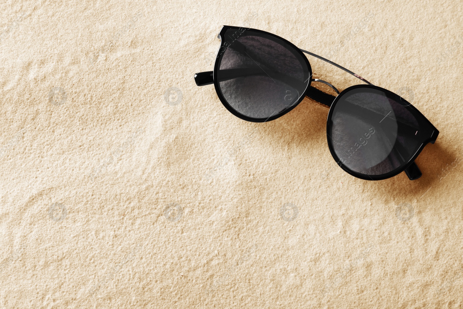 Photo of Stylish sunglasses on white sand, top view. Space for text