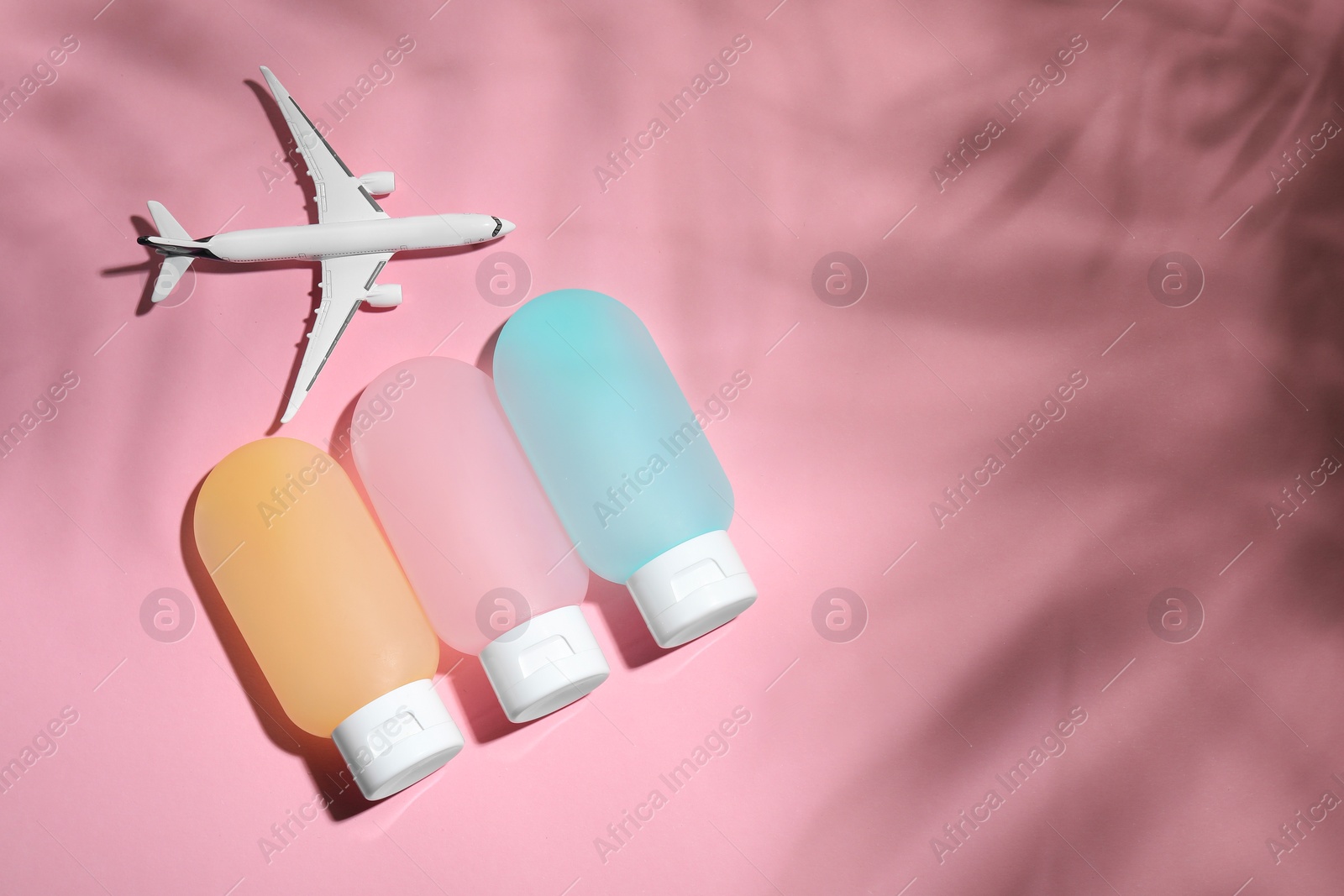 Photo of Cosmetic travel kit and toy plane on pink background, flat lay with space for text. Bath accessories