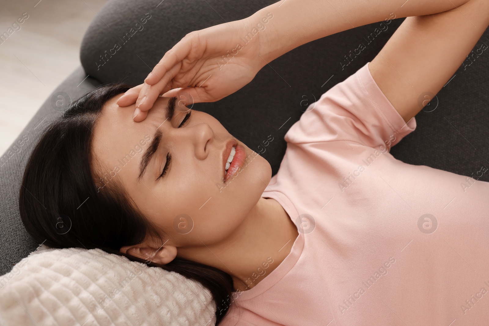 Photo of Sad woman suffering from headache on sofa indoors