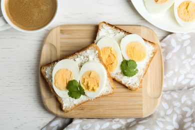 Tasty egg sandwiches served with coffee on white wooden table, flat lay