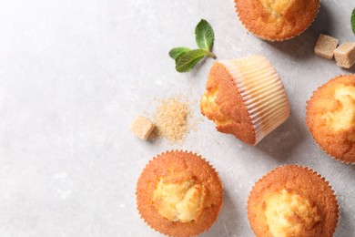 Delicious sweet muffins and brown sugar on light grey textured table, flat lay. Space for text