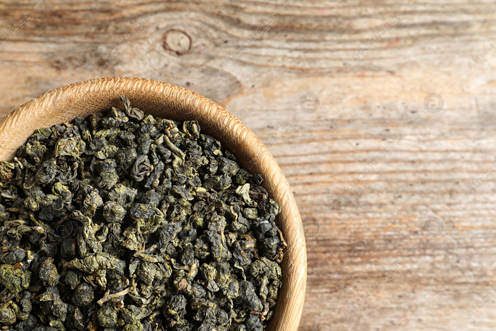 Photo of Bowl of Tie Guan Yin oolong tea leaves on wooden background, top view with space for text