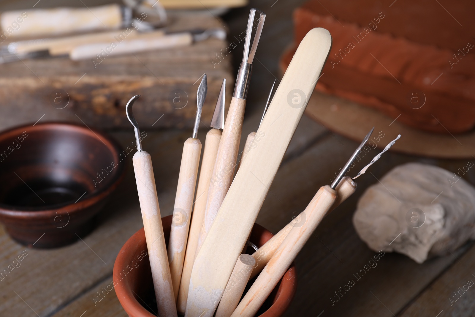 Photo of Set of different clay crafting tools on wooden table in workshop, closeup