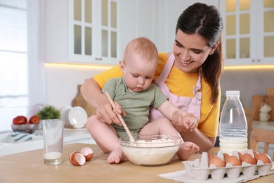Photo of Happy young woman and her cute little baby making dough together in kitchen, space for text