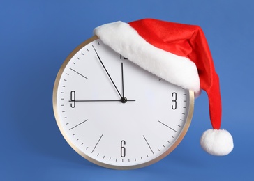 Photo of Clock with Santa hat showing five minutes until midnight on blue background. New Year countdown