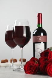 Photo of Bottle with glasses of red wine, beautiful roses and chocolate candies on white table