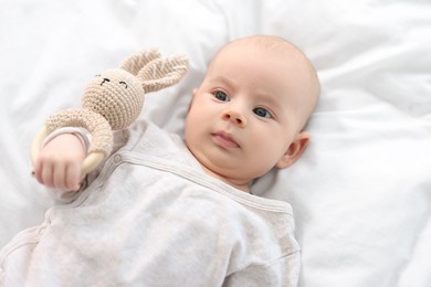 Photo of Cute little baby with toy lying on white sheets, top view