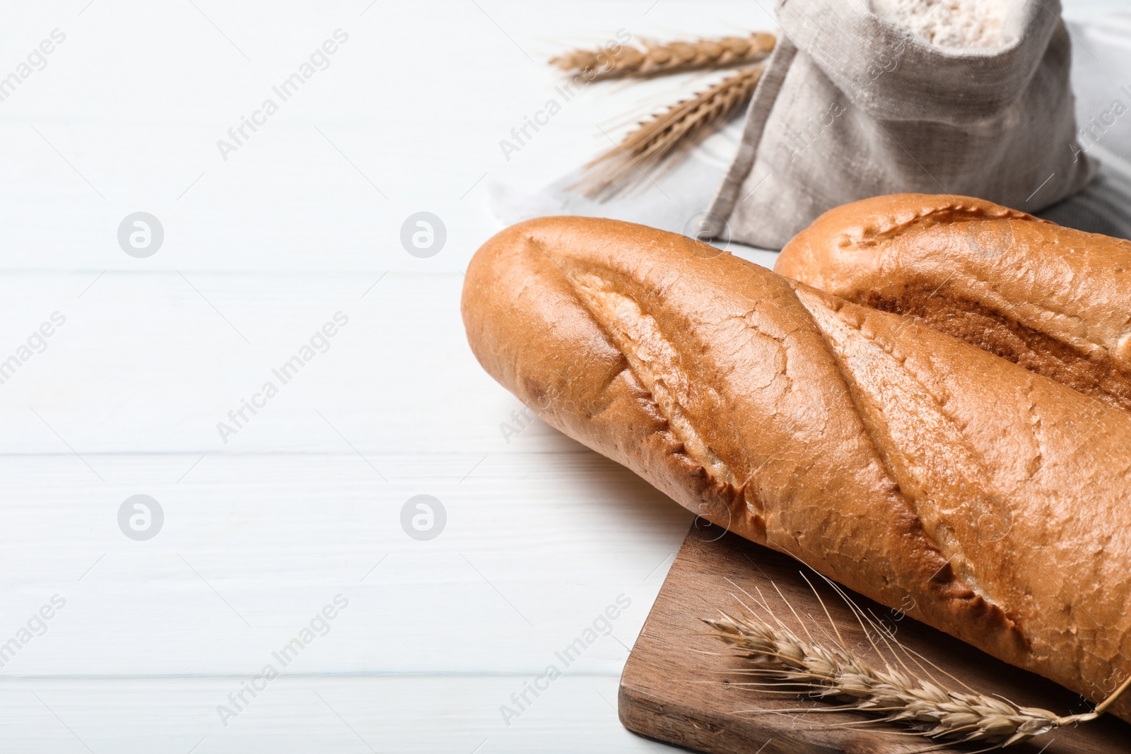 Photo of Fresh tasty baguettes, flour and spikelets on white wooden table, closeup. Space for text