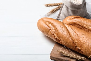 Fresh tasty baguettes, flour and spikelets on white wooden table, closeup. Space for text