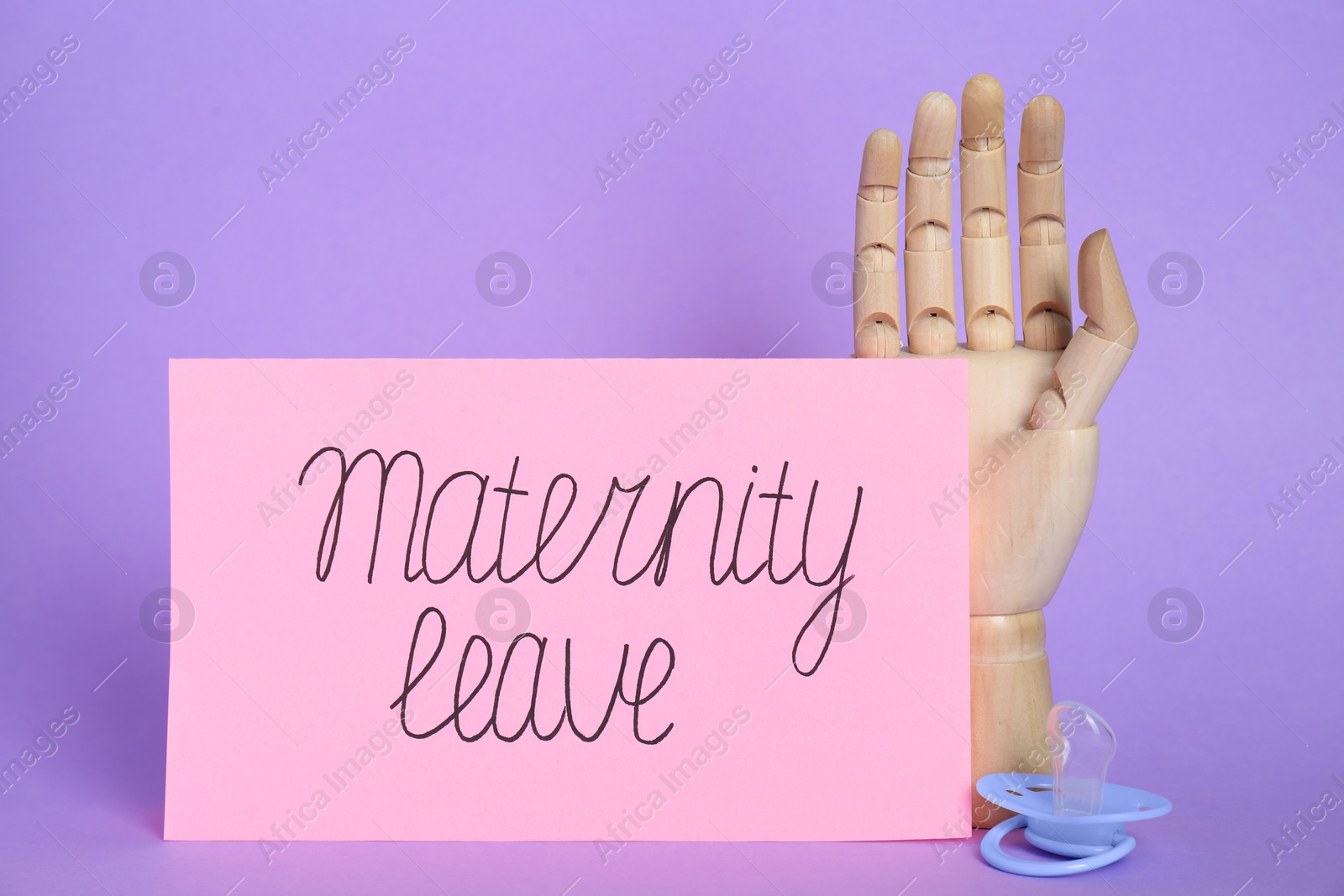 Photo of Wooden mannequin hand, card with phrase Maternity Leave and pacifier on violet background