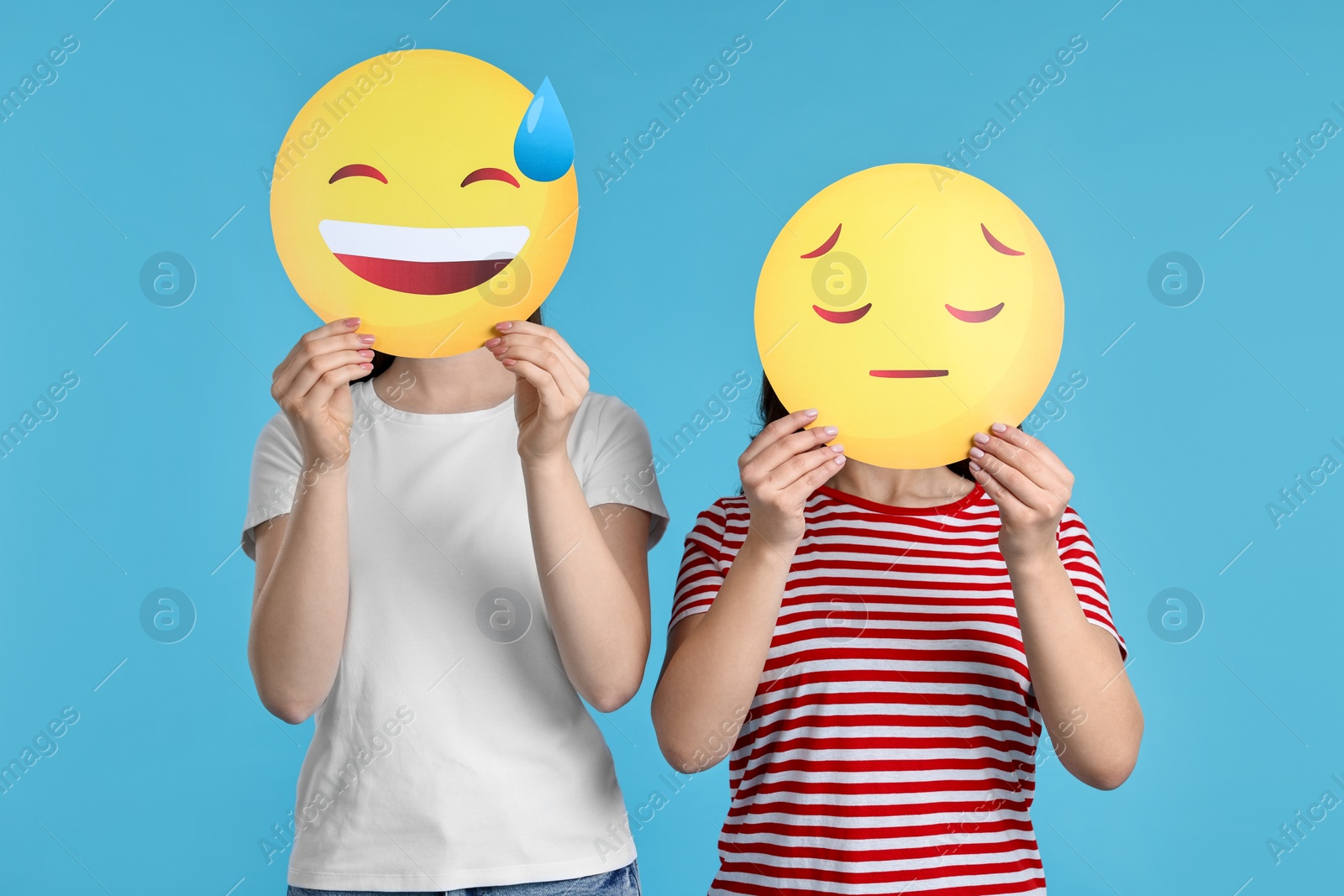 Photo of People covering faces with emoticons on light blue background