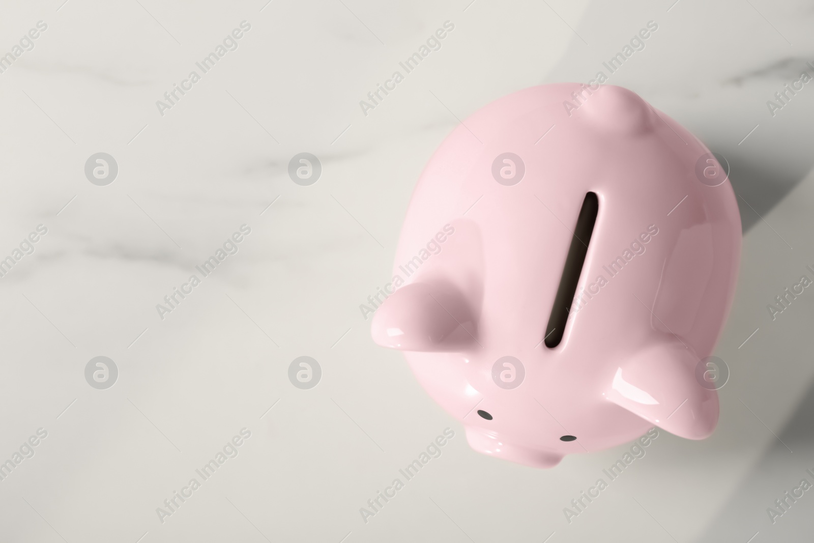 Photo of Ceramic piggy bank on white marble table, top view. Space for text