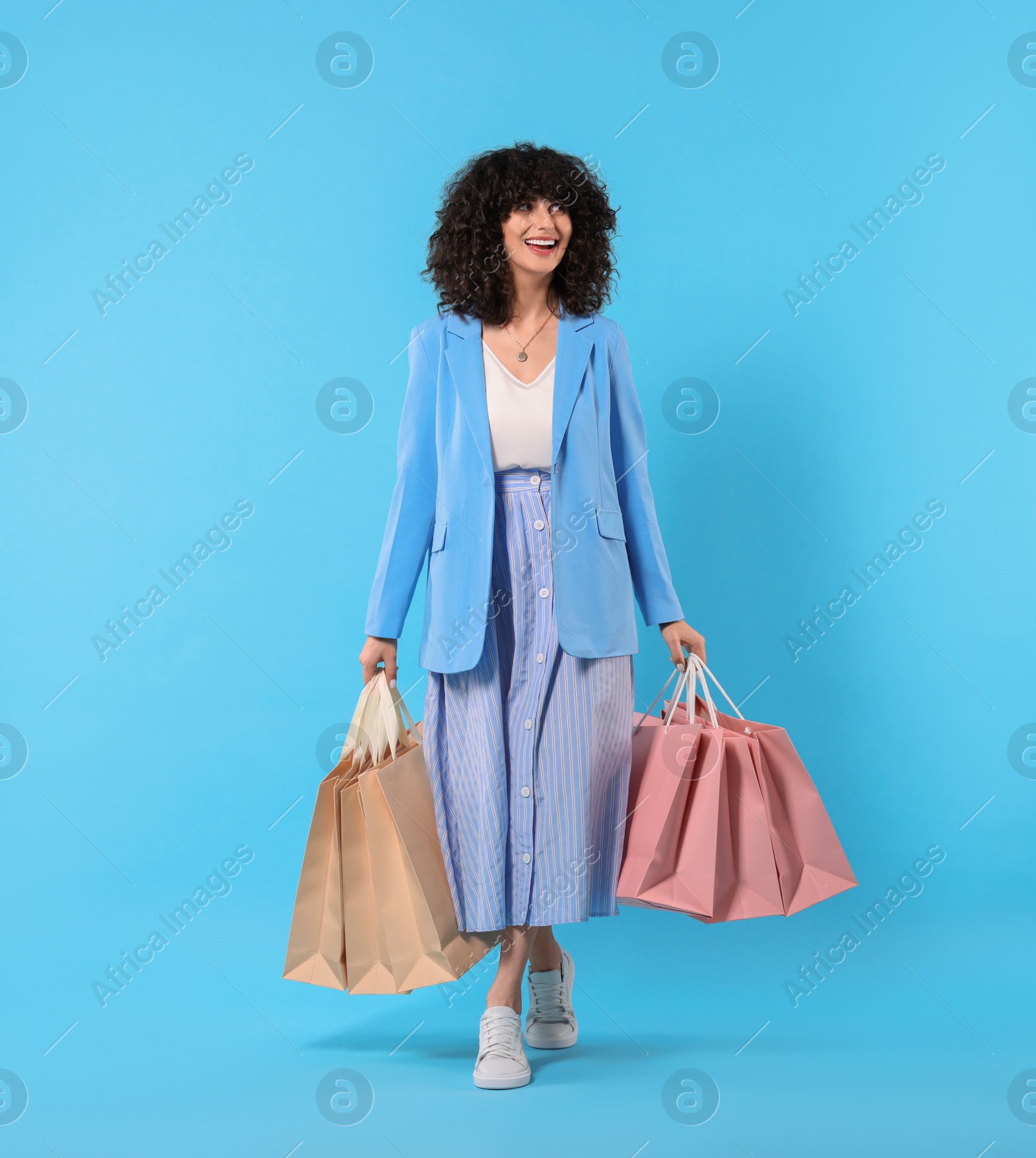 Photo of Happy young woman with shopping bags on light blue background. Space for text