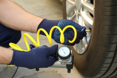 Photo of Mechanic checking air pressure in car tire outdoors, closeup