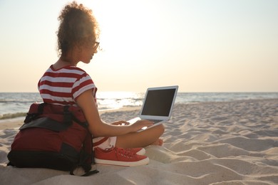 Photo of African American woman working on laptop at beach