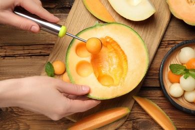 Woman making melon balls at wooden table, closeup