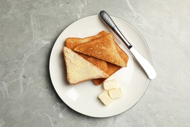 Photo of Tasty toasts with butter served on grey marble table, top view