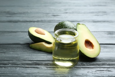 Photo of Jar of natural oil and avocados on grey wooden background