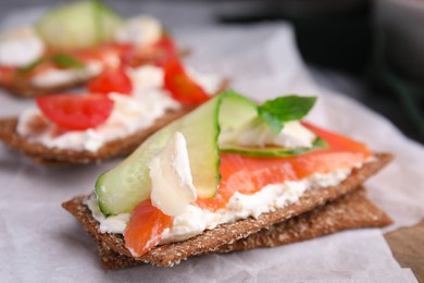 Photo of Tasty rye crispbreads with salmon, cream cheese and cucumber on parchment paper, closeup
